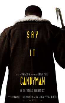 The Candyman faces opposite the viewer. On top of his large dark coat are the words "Say It" and "Candyman" in yellow font.