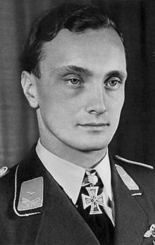 A young man with slightly curly hair wearing a military uniform and an Iron Cross shaped military decoration at his neck.