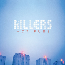 A set of buildings in blue, with red neon signs at the rooftops with Chinese characters. The album's title "Hot Fuss" appears in red text.