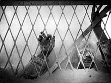 A black and white image of the film depicting the village doctor's hands and arms above flour as he presses up against a chain link fence.
