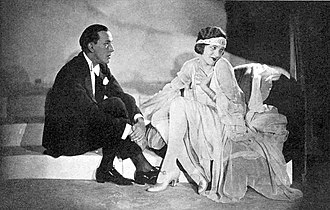A young white man, clean shaven, in evening costume, with a young white woman, both seated