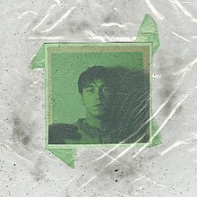 A green-colored photo of the artist on a white background smudged with dirt, under a sheet of clear plastic.