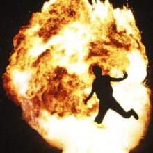 An image of a big explosion with a silhouette of a man in front of it.