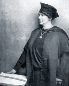 middle-aged white woman with dark hair, wearing academic cap and gown