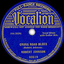 Photo of original 78 record label showing "Vocalion" in stylized lettering with "Cross Road Blues", "Vocal Blues with Guitar Acc[ompaniment]", and "Robert Johnson" as identifiers along with catalog numbers, "Made in USA", etc.