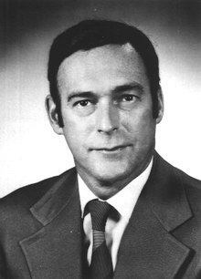 Headshot of a dark-haired, clean-shaven, middle-aged man wearing a suit