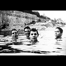 A black-and-white photograph of four men swimming in a quarry lake