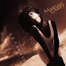 A brunette woman in a white low-cut minidress standing in front of a dark, sepia-toned desert-like background, hair flailing upward in the wind, the words "MARIAH CAREY" on the upper right hand side of the artwork and the word "EMOTIONS" vertically spelled out from the top down towards the bottom left hand side of the artwork.