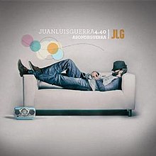 Juan Luis Guerra lying down on a couch with his hat covering his eyes. A blue and silver retro-styled radio is seen on the floor.