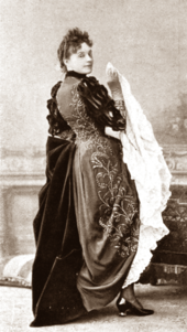 Young European woman in full length period costume (circa 1800?) in semi profile, looking over her right shoulder at the camera