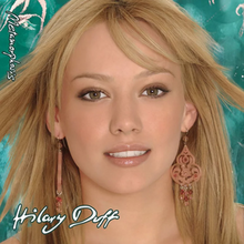 The face of a young blonde girl standing in front of a green background. She has brown eyes and is wearing brown-and-pink chandelier earrings. On her image, the words "Hilary Duff" and "Metamorphosis" are written in white, cursive print.