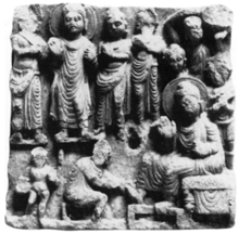 Ancient relief showing the Buddha standing surrounded by several monks in the upper part, with one monk hurling a boulder at the far right. Below a man is kneeling and holding the feet of the Buddha, while a child is standing behind the kneeling man, holding some object.