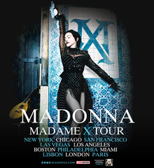 Madonna wearing a black dotted dress, holding a bottle of wine with her arm up, against a wall with a Qashani of "Madame X" logo.