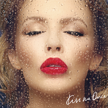 A face portrait of Minogue kissing a clear glass screen, with water droplets running down. A blue-ish background is behind the woman, with the text "Kiss Me Once" present on the bottom right corner.