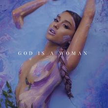 Grande emerging from a pool of blue and purple paint, wearing body paint of the same colors. A few leaves can be seen on the bottom left corner of the image. The song title "God Is a Woman" is displayed at the center of the cover art, stylized in all caps and in a white font.