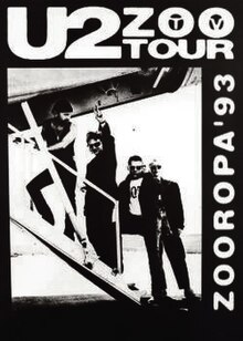 A black poster with a black-and-white image occupying most it. The image shows U2 walking up the stairs of a small aeroplane as Bono gives a peace sign towards the viewer. Text on the poster reads "U2 Zoo TV Tour" and "Zooropa '93".