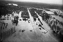 Aerial photo showing large swaths of land and homes flooded by a swollen river.