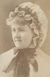 Young white woman in 19th-century dress including a frilly cap, as worn by maids in domestic service