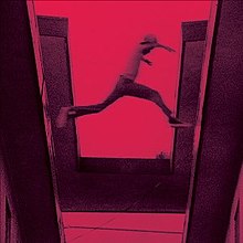 A red-tinted film still showing a boy jumping from one roof to another