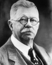 An early 20th-century photo of a middle-aged man with glasses, a mustache, and a suit.