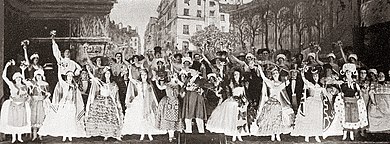 large stage with large cast in mid-19th century costume in an ensemble number, with the market of Les Halles behind them