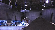 A studio sound stage, with a pile of mulch in the foreground and cherry pickers and a constructed mausoleum in the background.
