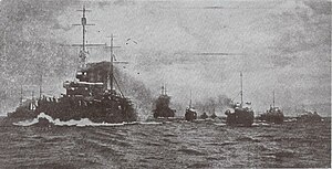 A line of battleships steams through the sea, with smoke rising from their funnels.