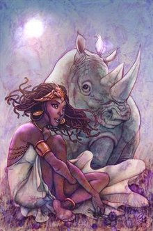 An elegant African woman with long dreadlocks poses sitting in front of a rhinoceros