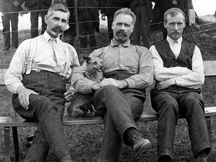 A group of three men seated on a wooden bench
