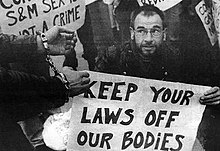 Image shows a man holding a sign reading "Keep Your Laws Off Our Bodies", while another man wears a set of handcuffs