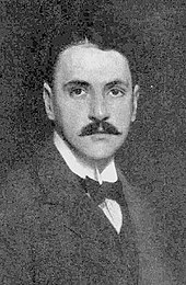 young man with neat dark hair and moustache, wearing a wing-collar and bow-tie in a dark suit