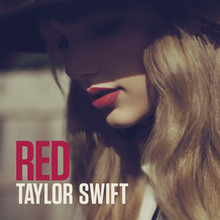 A closeup of Taylor Swift donning red lipstick with her face, half-covered by a brimmed hat, looking downwards