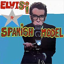 A younger man wearing glasses behind a camera with the words "ElvisI" and "Spanish Model"