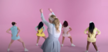 Four women twerking and one standing still in front of pastel-colored pink backdrop.